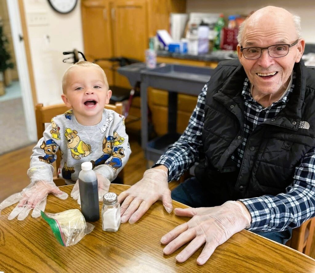 A little boy smiling with a senior man while they mix ingredients together